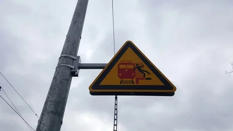 Triangular caution sign man falls of platform in front of train, pole, cloudy Stockbeeldmateriaal 76495215