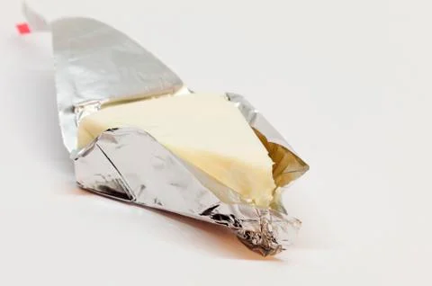 A triangular cheese wrapped in silver foil on white background Stock Photos