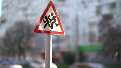 Triangular children crossing warning sign on a white pole against a blurred Vídeo Stock 348431079