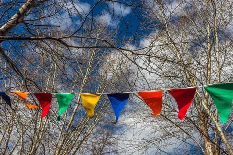 The triangular colored flags hang on a white rope between the branches of trees Foto stock