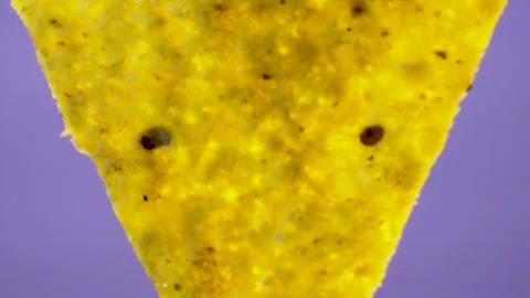 Triangular corn nacho chip with salt crystals rotating on purple background Stock Footage 345610780