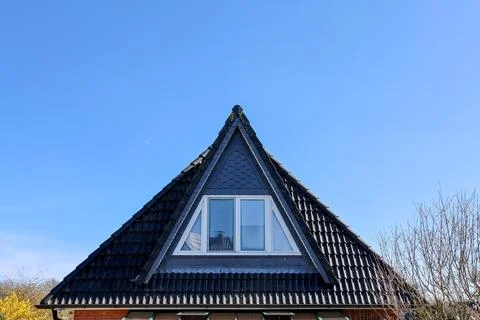 Triangular dormer window with black roof tiles and blue sky 스톡 사진