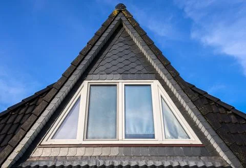 Triangular dormer window with slate roof tiles against blue sky 스톡 사진