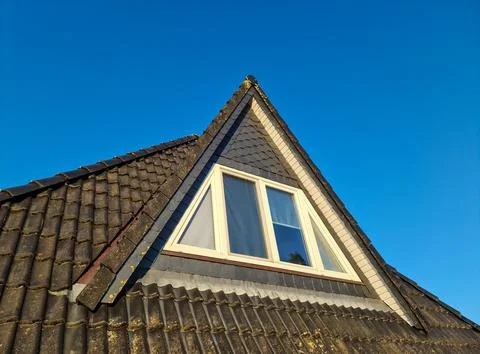 Triangular dormer window on a tiled roof against blue sky Stock Photos