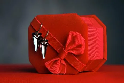 Triangular earrings on a red gift box on a dark background. Jewelry for women Stock Photos