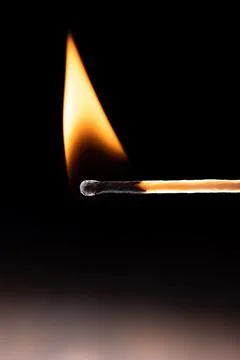 Triangular flame on a burning match against a black background. Stock Photos