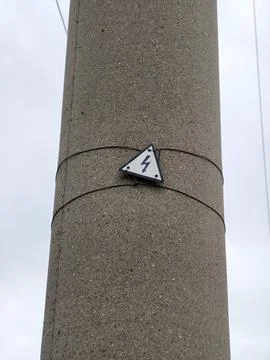 Triangular high-voltage warning sign mounted on grey concrete electricity p.. Stock Photos