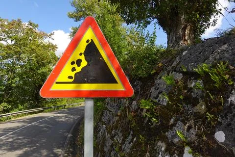 A triangular landslide warning sign stands beside a rural road, near a ston.. Stock Photos