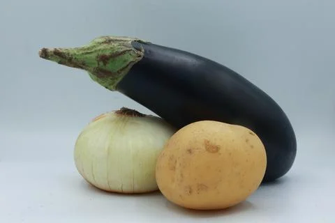 Triangular layout of eggplant, white onion, and potato on a neutral Stock Photos