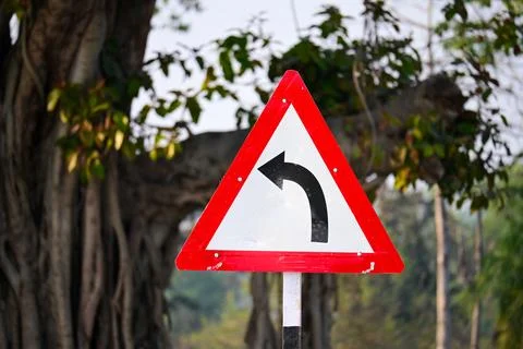 Triangular Left Curve Road Sign with Red Border in Natural Outdoor Setting Stock Photos