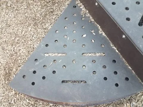 Triangular metal structure in shape of face with holes and wood chips Foto stock