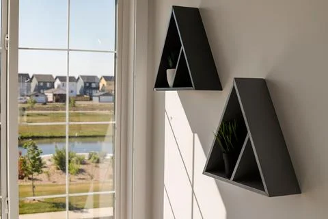 Triangular modern shelves hanging on a white wall near a window 写真素材