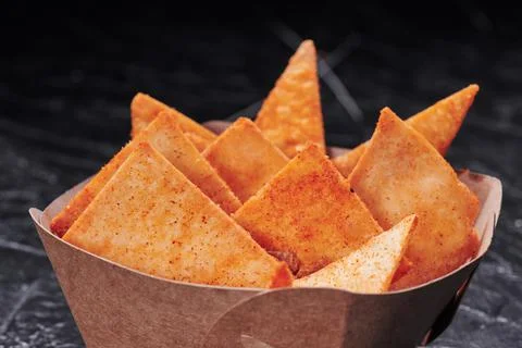Triangular nachos in a craft container on an isolated dark background. Photo for Stock Photos