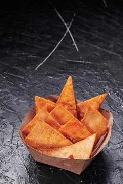 Triangular nachos in a craft container on an isolated dark background. Photo for Stock Photos