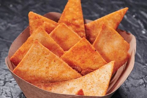 Triangular nachos in a craft container on an isolated dark background. Photo for Stock Photos