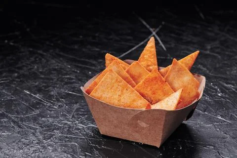 Triangular nachos in a craft container on an isolated dark background. Photo for Stock Photos