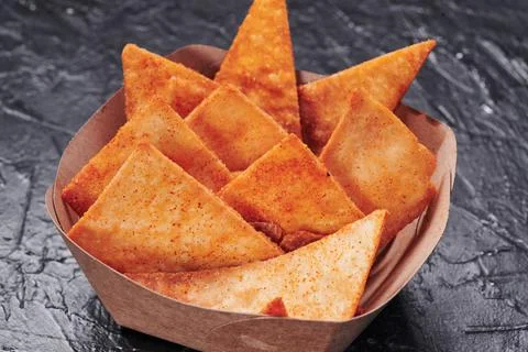 Triangular nachos in a craft container on an isolated dark background. Photo for Stock Photos
