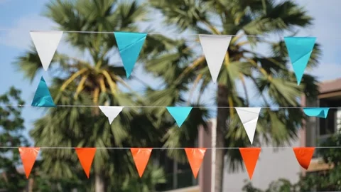 Triangular party flags waving against blue sky festive palm tree tropical Stock Footage 323483992