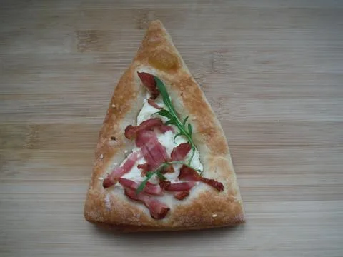 Triangular patty with ham, cheese and herbs on a wooden table. Foto stock