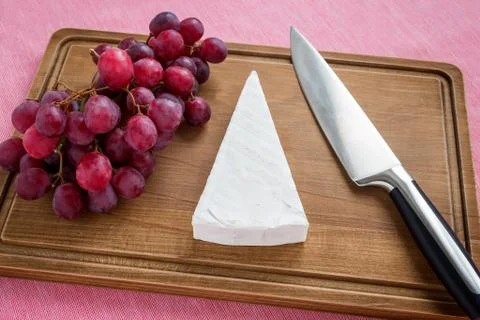 Triangular piece of Brie cheese, red sweet grapes and chef knife Foto stock