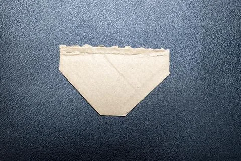 A triangular piece of brown paper with a torn edge rests on a black surface, Stock Photos