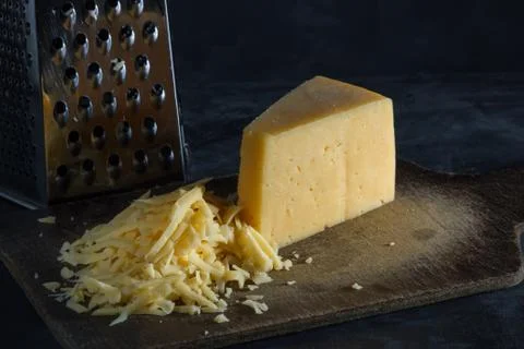 Triangular piece of cheese and grated cheese on a board Stock Photos