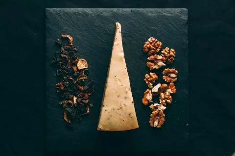 A triangular piece of cheese on a slate plate with mushrooms and walnuts on t Stock Photos