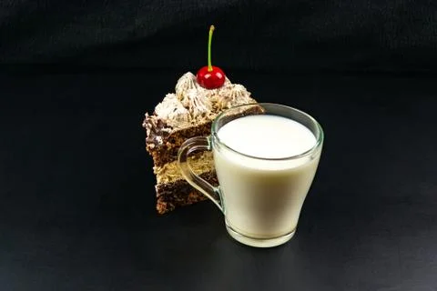 A triangular piece of tiramisu decorated with cherry, a glass cup with milk. Stock Photos