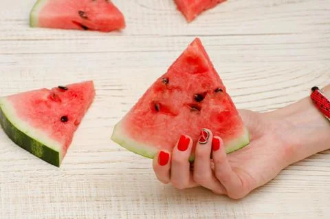 Triangular piece of watermelon in a female hand with a manicure on a light wo Stock Photos