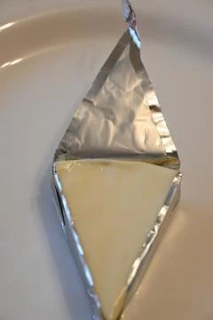 Triangular portion of processed cheese in opened foil wrapper Stock Photos