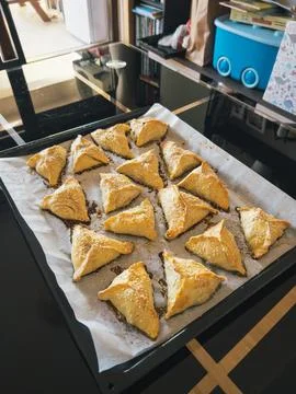 Triangular puff pastry pies lie on a tray on the table Stock Photos