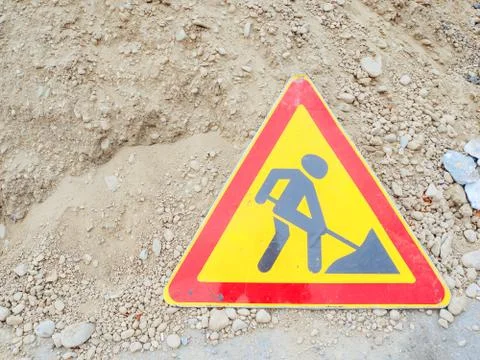 Triangular red-yellow road sign with a picture of a digging man stand near a Stock Photos