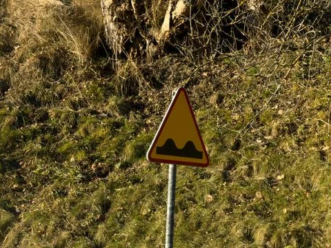 A triangular road sign indicating uneven terrain or road bumps stands against a Stock Photos