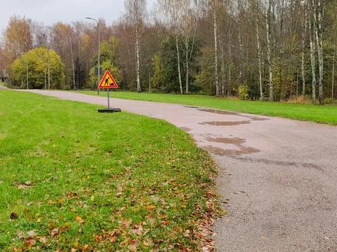 A triangular road work sign warning of construction is placed on a metal base Stock Photos