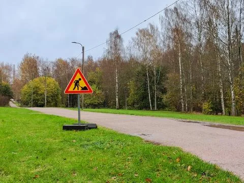 A triangular road work sign warning of construction is placed on a metal base Stockfoto's