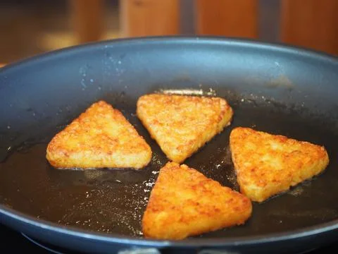 Triangular roesti corners fried in the pan darkly Stock Photos