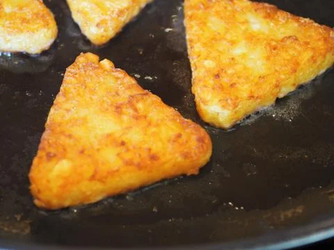 Triangular roesti corners fried in the pan darkly Stock Photos