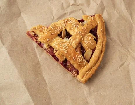 Triangular slice of baked cherry pie on brown paper Stock Photos