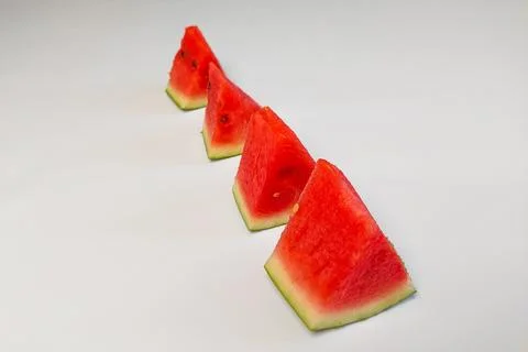 Triangular slices of fresh red watermelon arranged in rows against a white .. Stock Photos