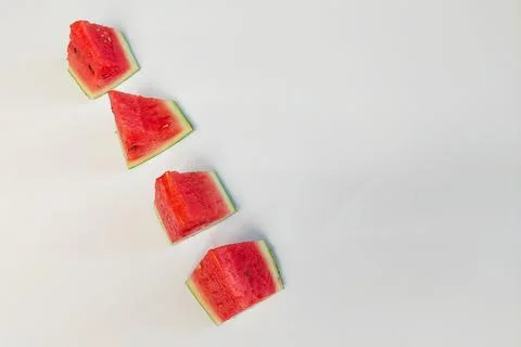 Triangular slices of fresh red watermelon arranged in rows against a white .. Stock Photos