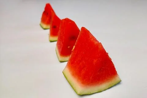 Triangular slices of fresh red watermelon arranged in rows against a white .. Stock Photos