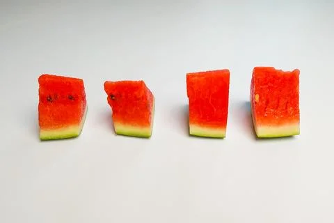 Triangular slices of fresh red watermelon arranged in rows against a white .. Stock Photos
