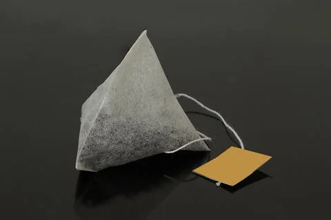 Triangular tea bag on a black background. Stock Photos
