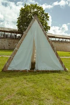 A triangular tent stands on green grass with a tree nearby Stock Photos