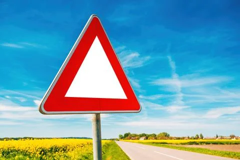 Triangular warning sign by the country road in cultivated canola field Stock Photos