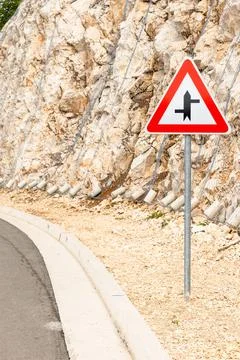 A triangular warning sign stands beside a curved road at a rocky hillside Stock Photos