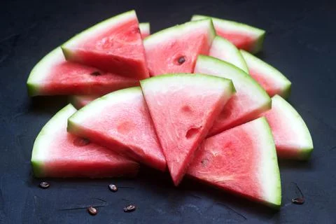 Triangular watermelon slices with seeds on a black concrete background. Foto stock