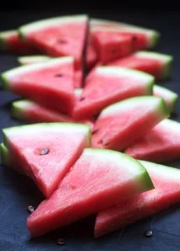 Triangular watermelon slices with seeds on a black concrete background. Stockfoto's