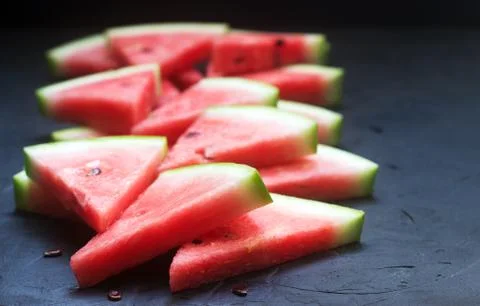 Triangular watermelon slices with seeds on a black concrete background. 스톡 사진