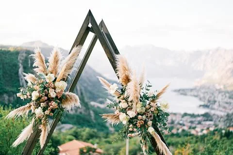 Triangular wedding tipi arch decorated with flowers stands on a mountain above Stock Photos